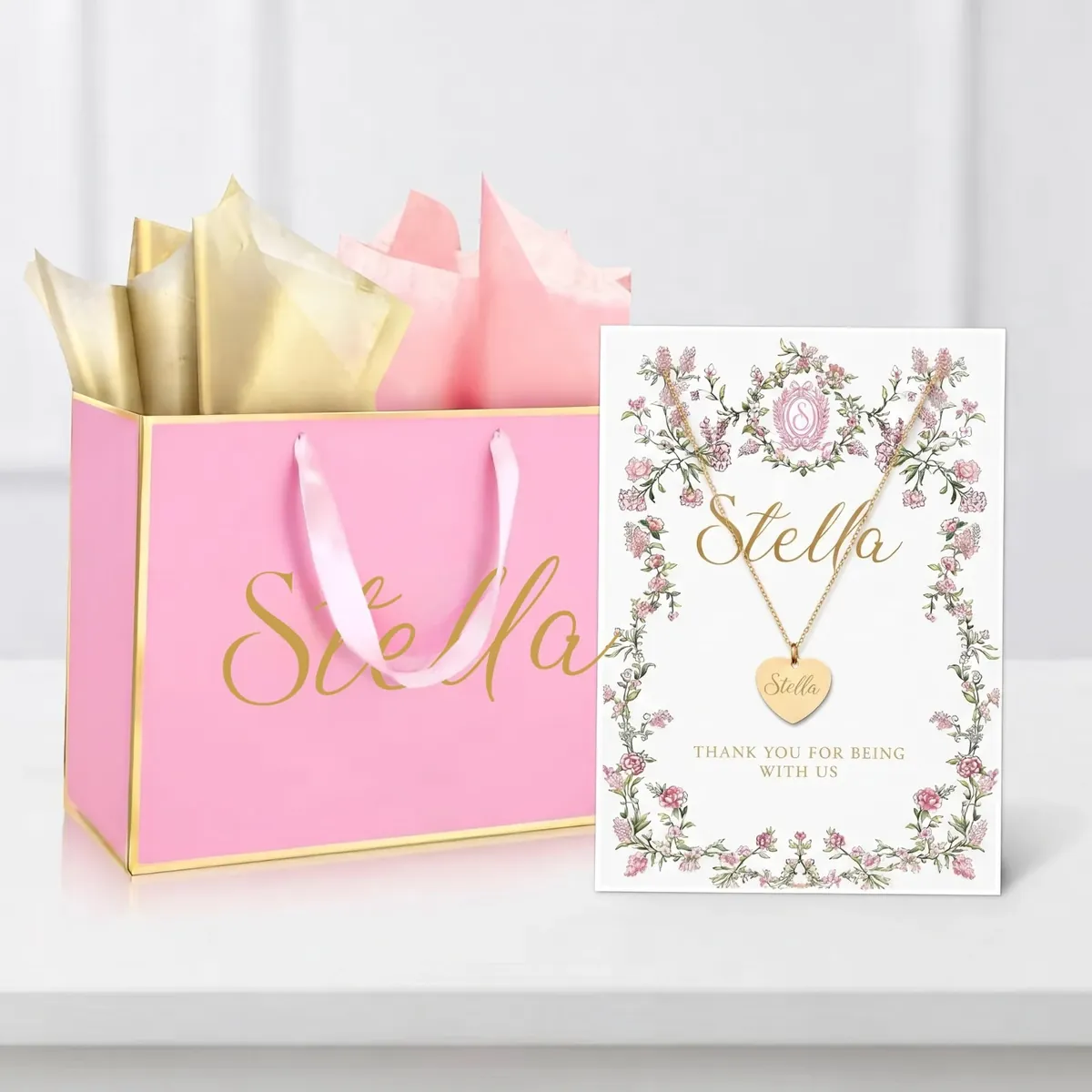 Pink gift bag with a name in gold and a floral card holding an engraved heart necklace