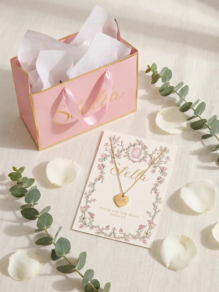 Pink gift bag with tissue paper and a floral card with the necklace